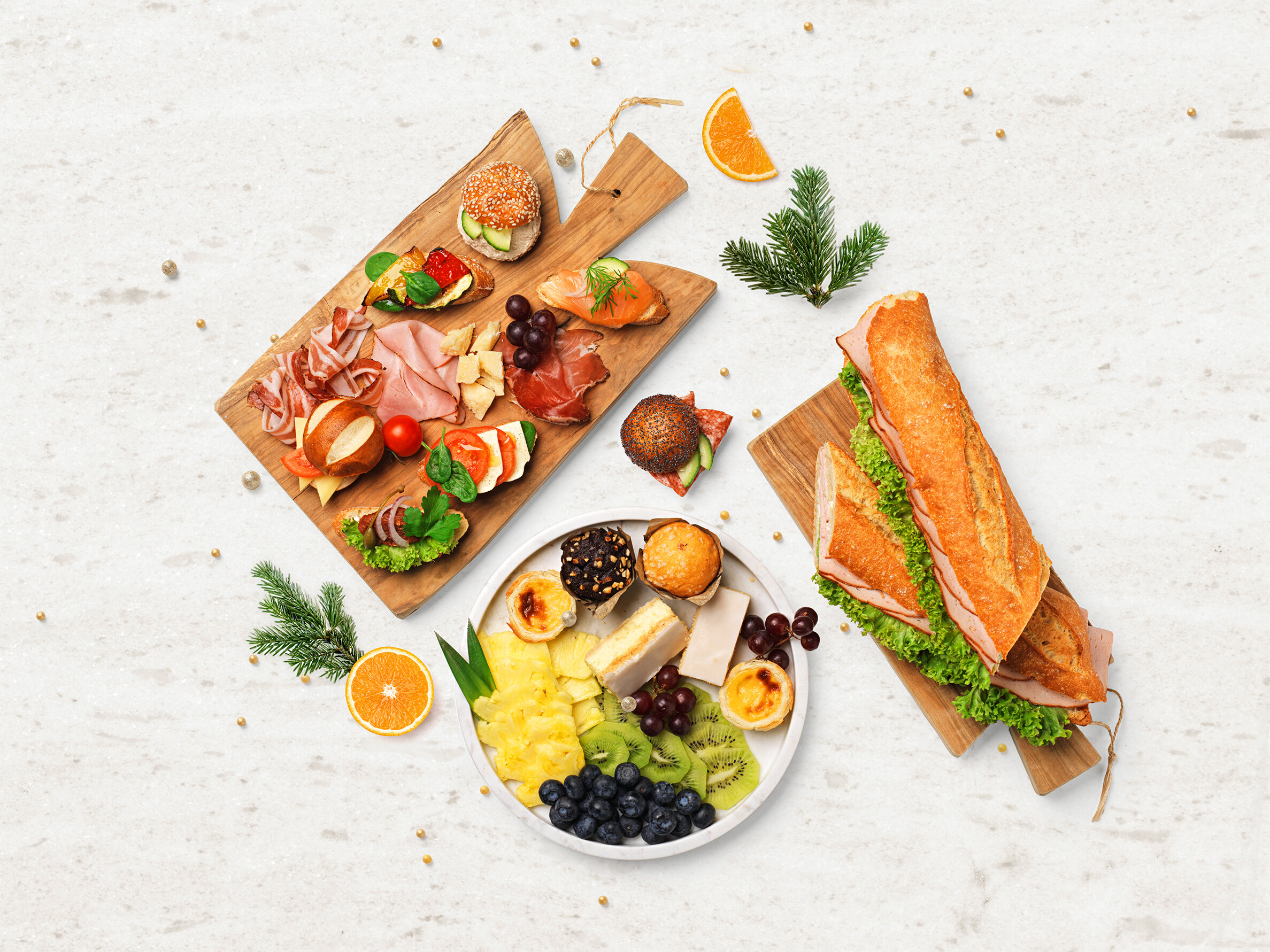 Festlich angerichtete Partyplatten mit Canapés, Käse, Früchten, Fleischspezialitäten und belegtem Baguette auf Holzplatten.